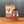A jar of Tradition Spice Company Honey Habanero Dry Rub Seasoning stands in front of a kraft paper pouch of the same seasoning on a wooden surface against a dark gray background.