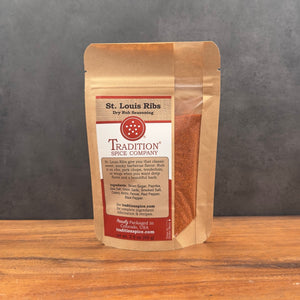 A stand-up pouch of Tradition Spice Company St. Louis Ribs dry rub seasoning, standing on a wooden surface against a dark gray background.