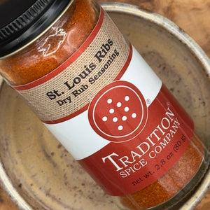 A close-up of a spice jar labeled 'St. Louis Ribs Dry Rub Seasoning' by Tradition Spice Company, placed inside a ceramic dish.