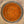 Top-down view of a spice blend inside a clear glass jar, showing a textured mix of orange, brown, and reddish seasoning on a speckled beige countertop.