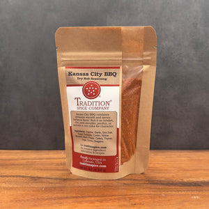 A stand-up pouch of Tradition Spice Company Kansas City BBQ Dry Rub seasoning, displayed on a wooden surface against a dark gray background.