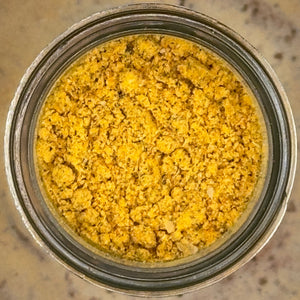 A top-down view of a clear glass jar filled with a coarse yellow-orange powder, set on a speckled beige countertop.