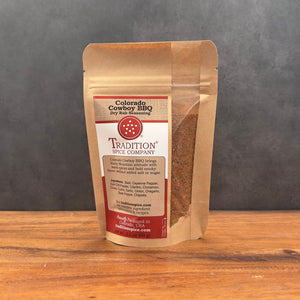 A stand-up pouch of Tradition Spice Company Colorado Cowboy BBQ Dry Rub seasoning, displayed on a wooden surface against a dark gray background.