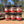 Six jars of Tradition Spice Company spices stacked on a wooden surface with a blurred outdoor background.