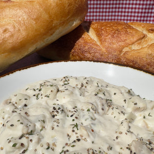 White plate with creamy mushroom sauce and bread on a checkered tablecloth